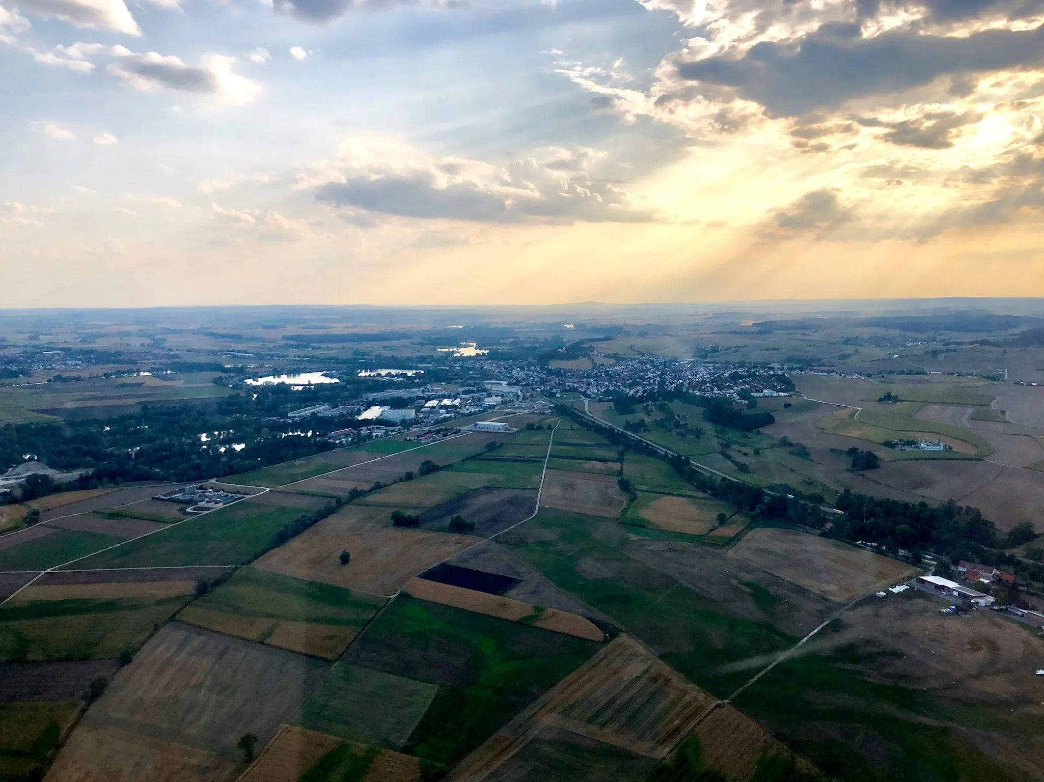 An aerial view over patchwork farmland, sun rays breaking through cloud.