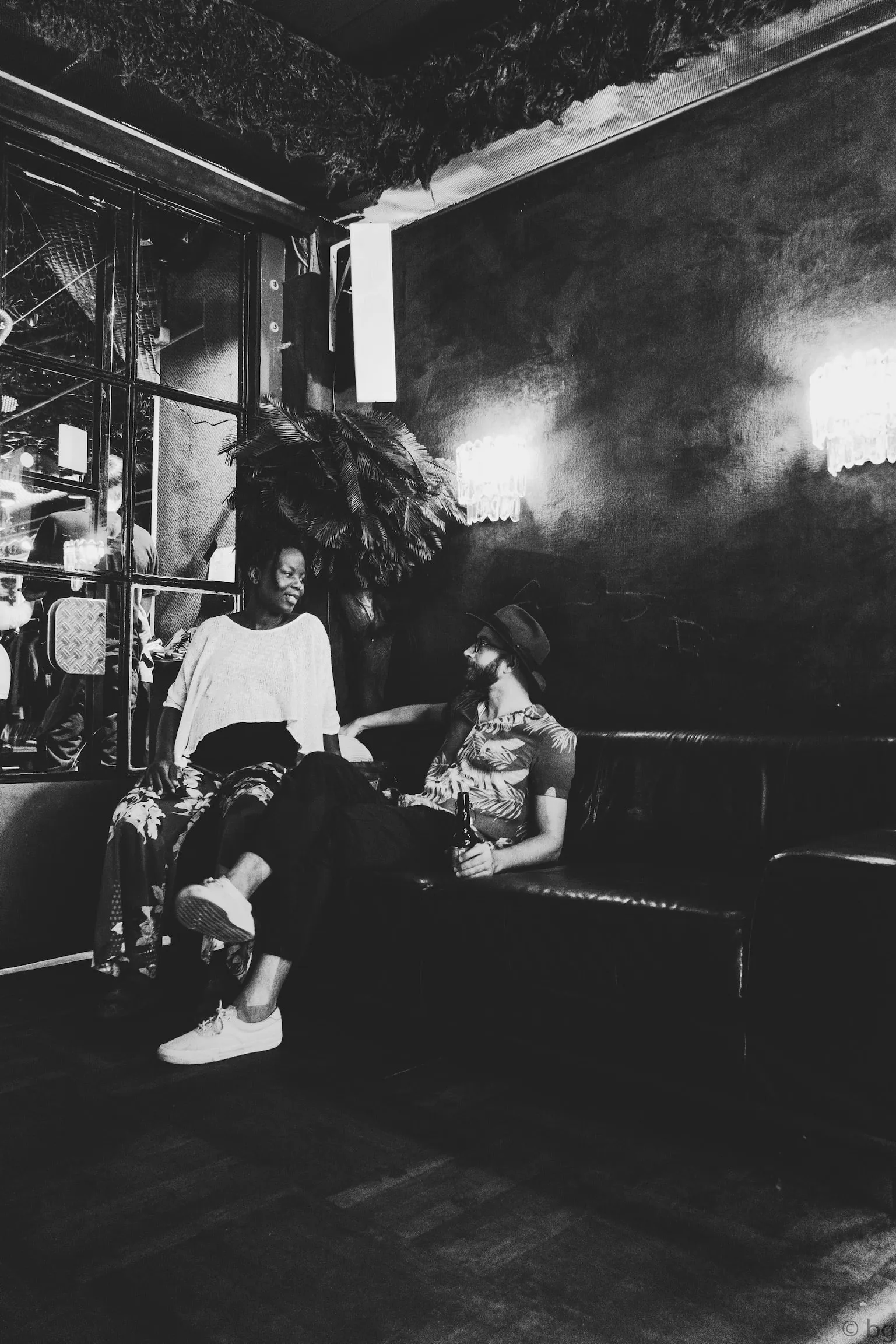 Black and white: two people talking in a large industrial hall lit by a bright window.