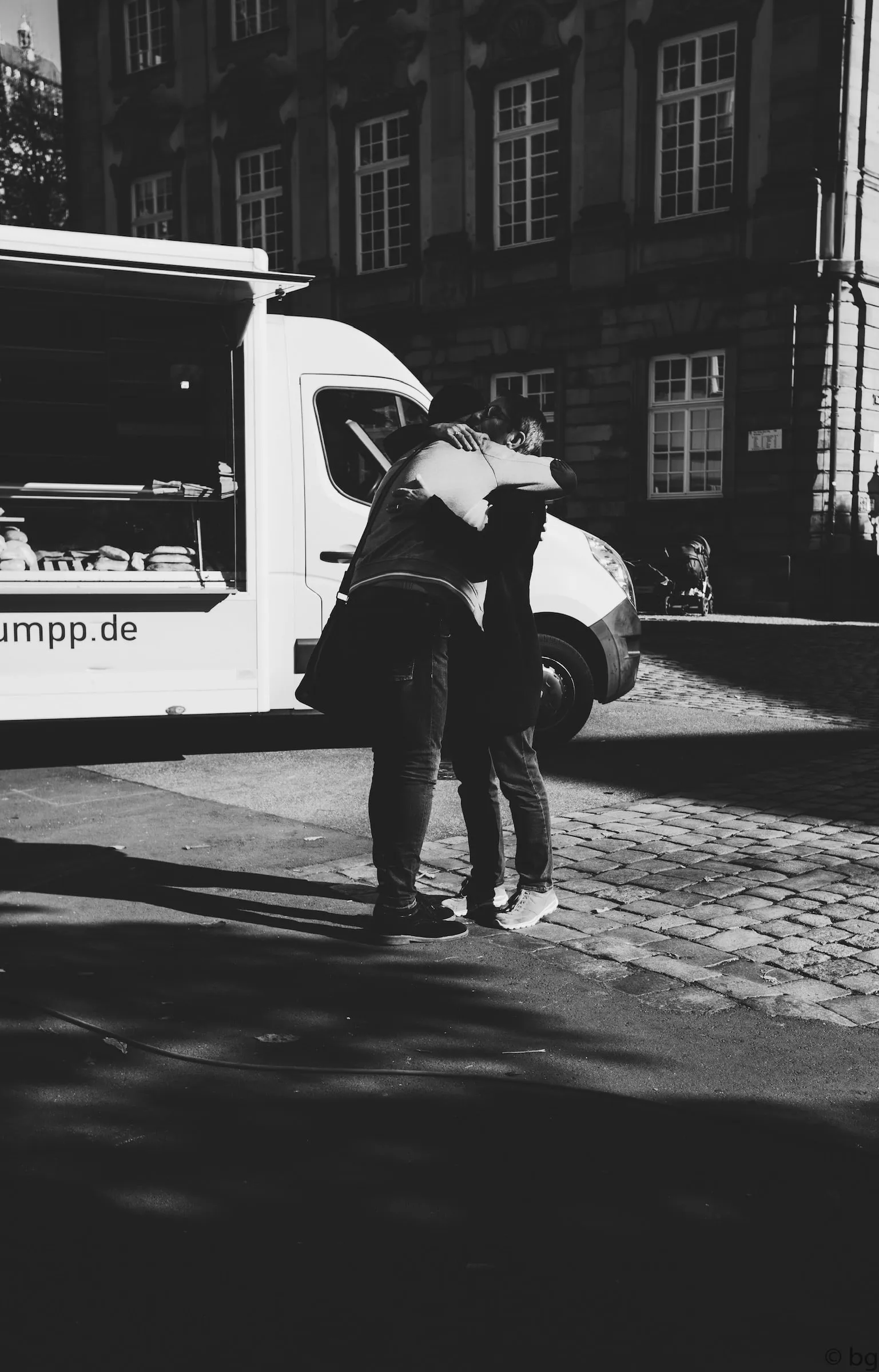 Two people embracing on a street beside a parked van.