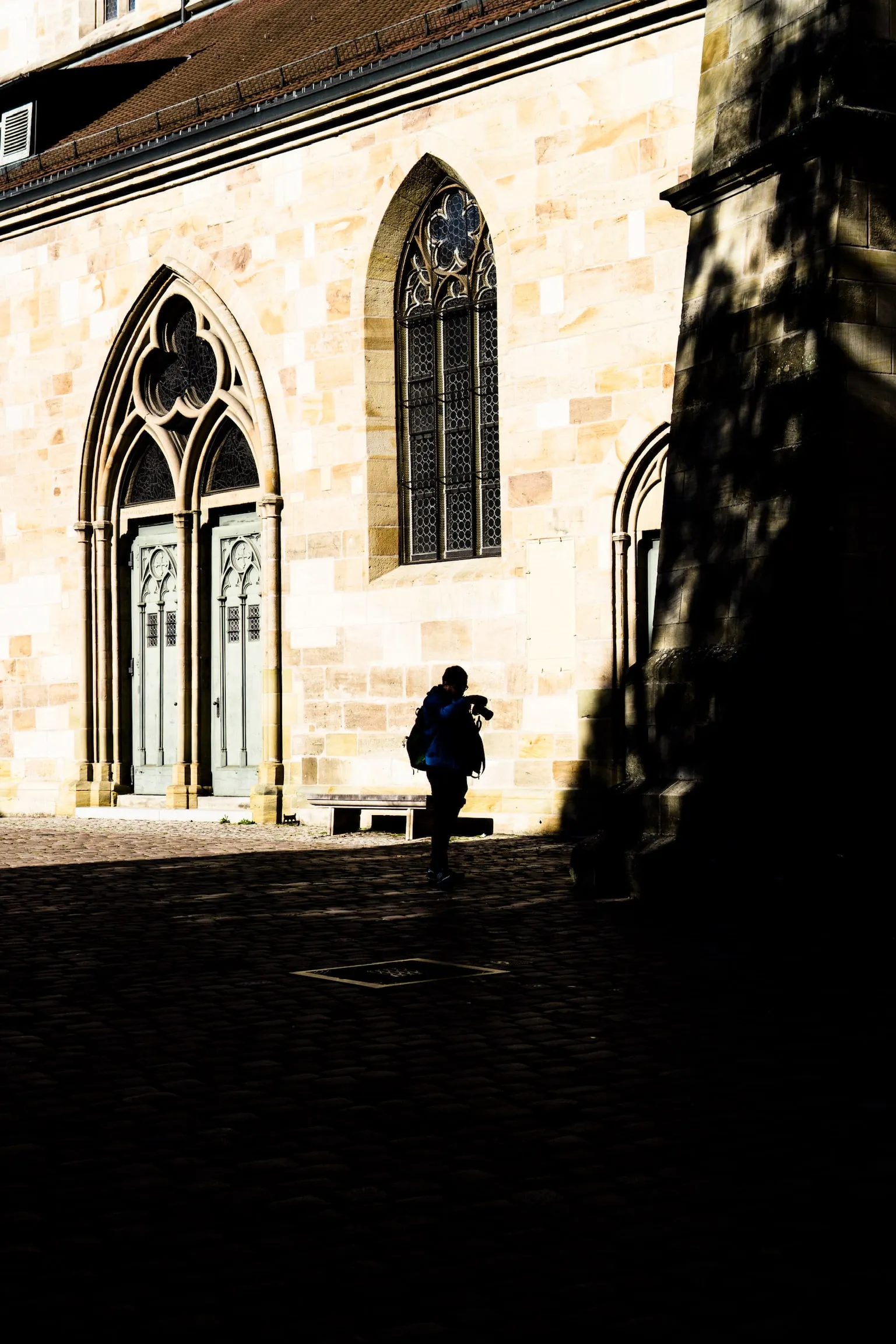 Gothic church windows catching low sunlight, with a small figure standing in the shadow below.