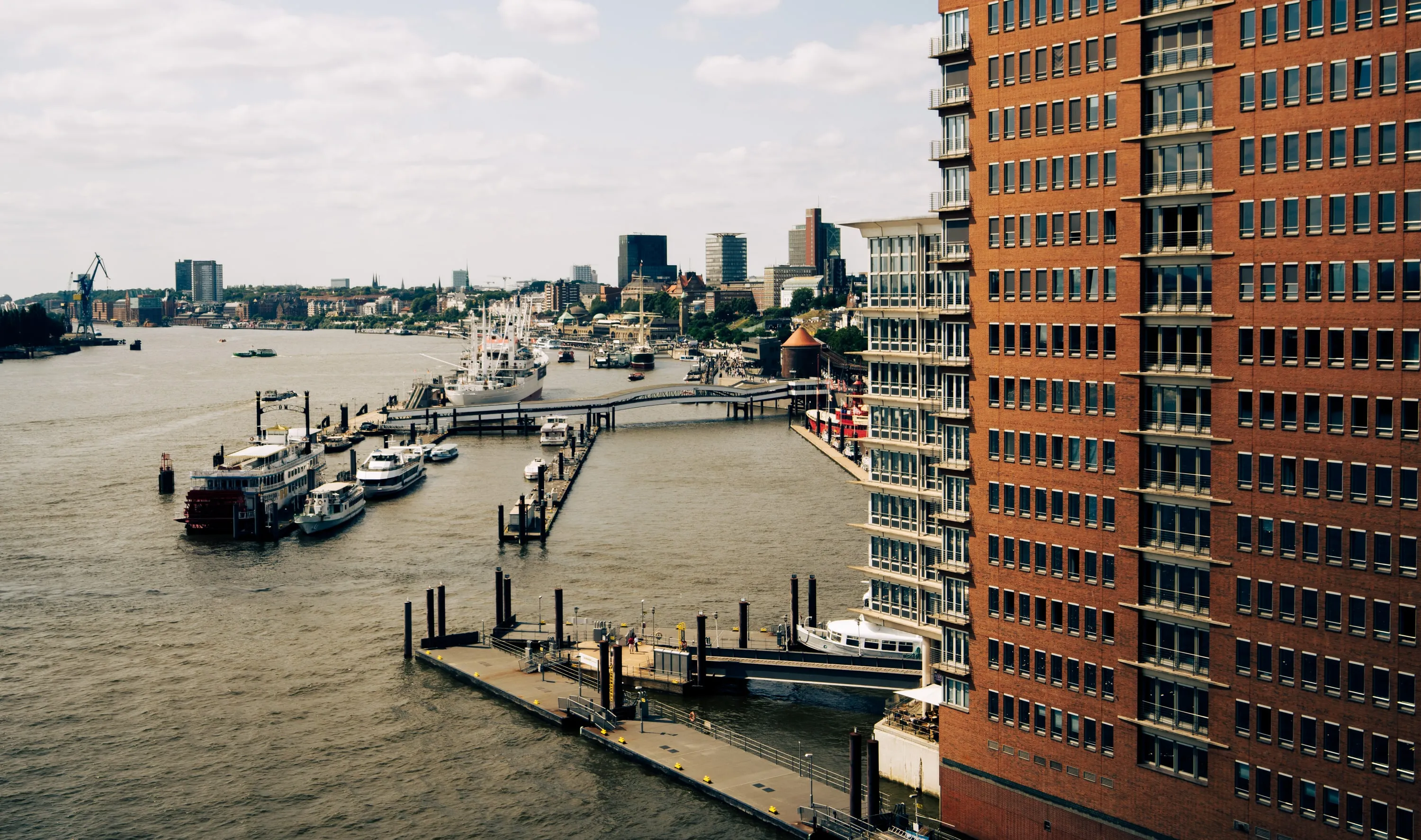A harbour lined with modern brick buildings, boats moored along the quay.