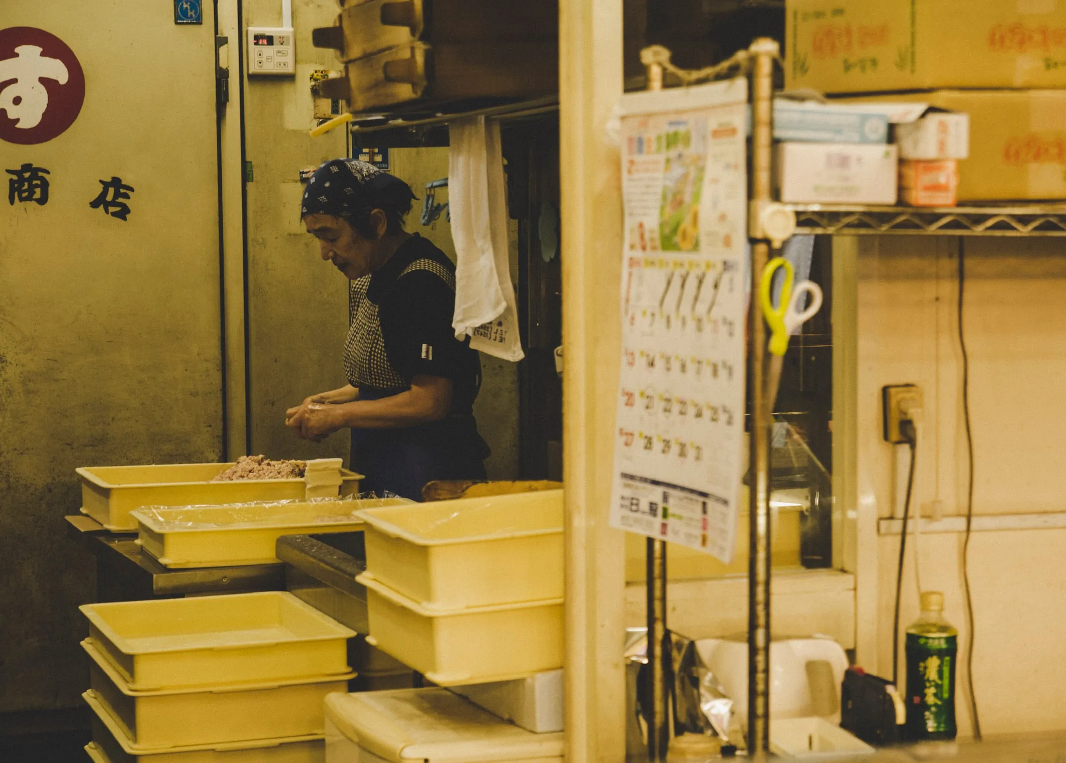 A market kitchen stacked with yellow crates, a worker at the counter.