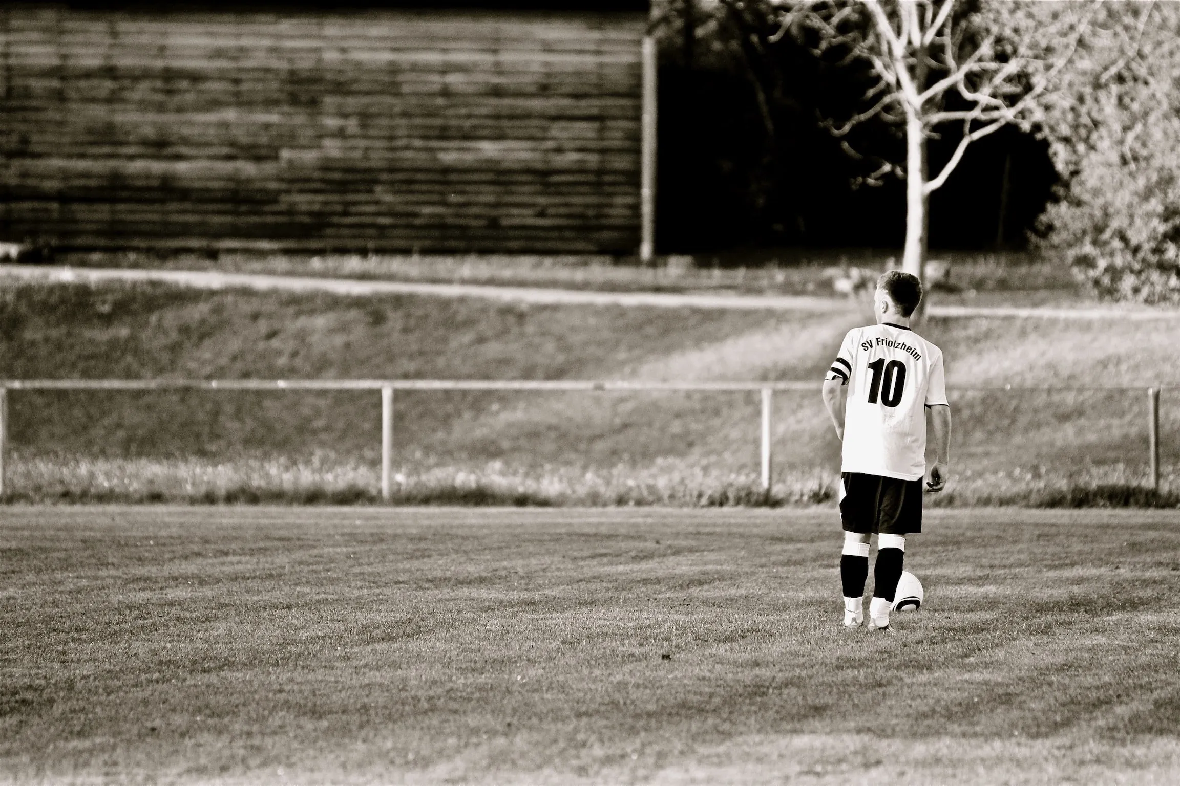 A lone footballer in a number ten shirt standing on an empty pitch.