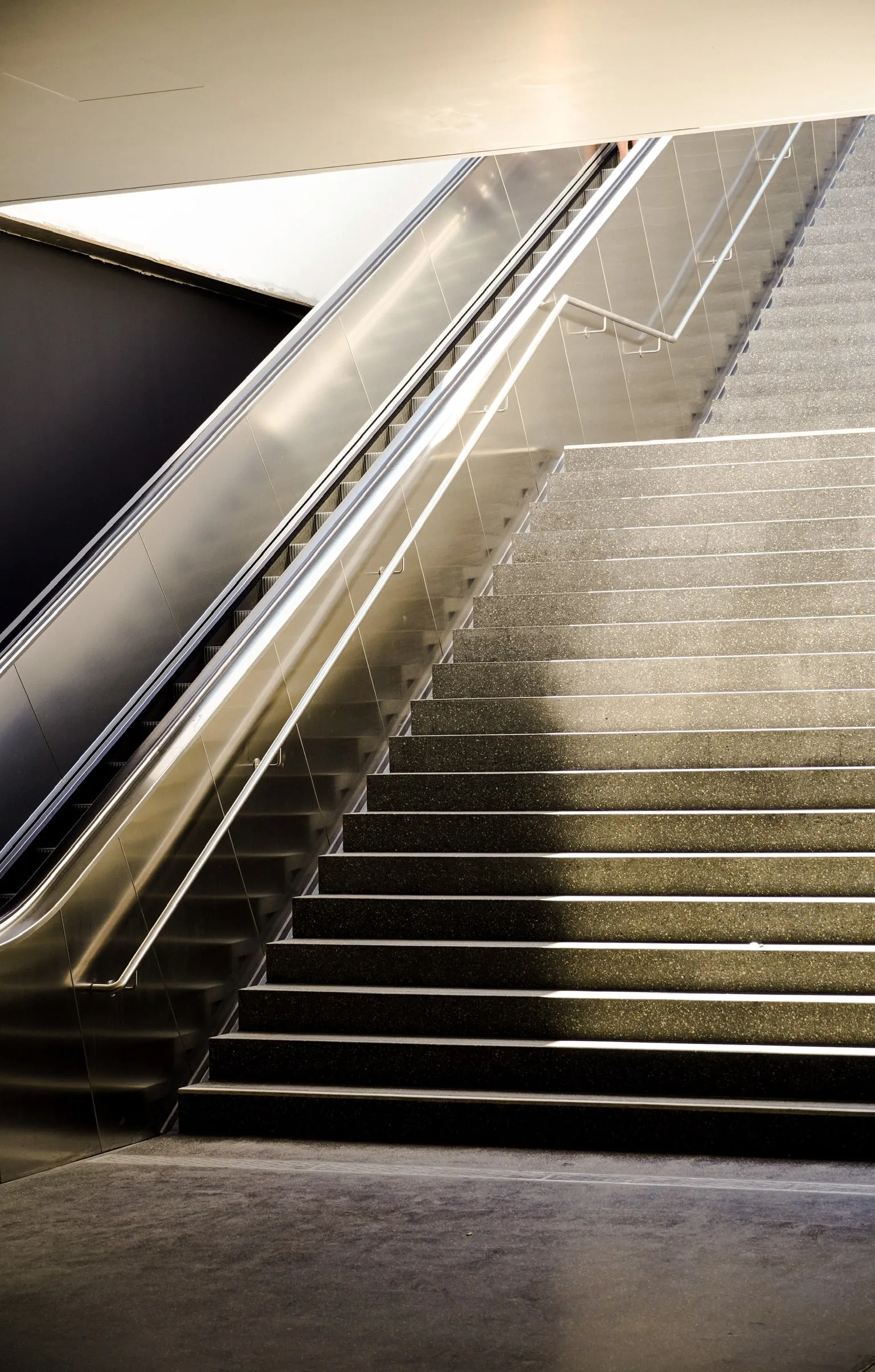 A stairway and escalator meeting in strong diagonals under hard light.